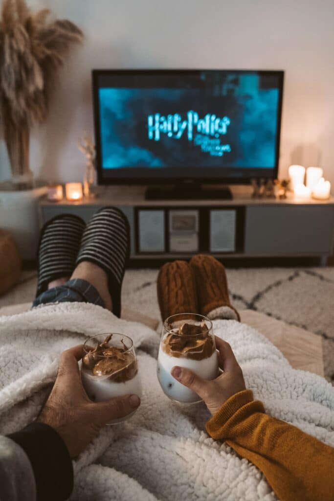 Photo of a couple snuggled on a couch, holding drinks, watching a Harry Potter movie on TV