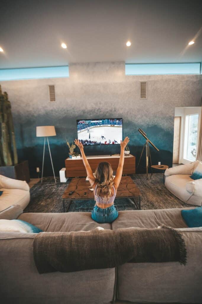 A woman sitting on a couch cheering, watching hockey on TV.