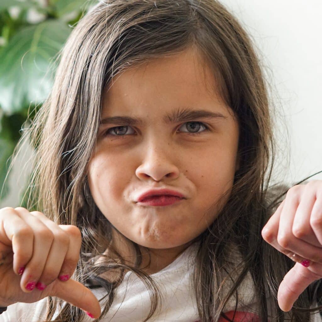 Photo of a young girl making a face and giving two thumbs down