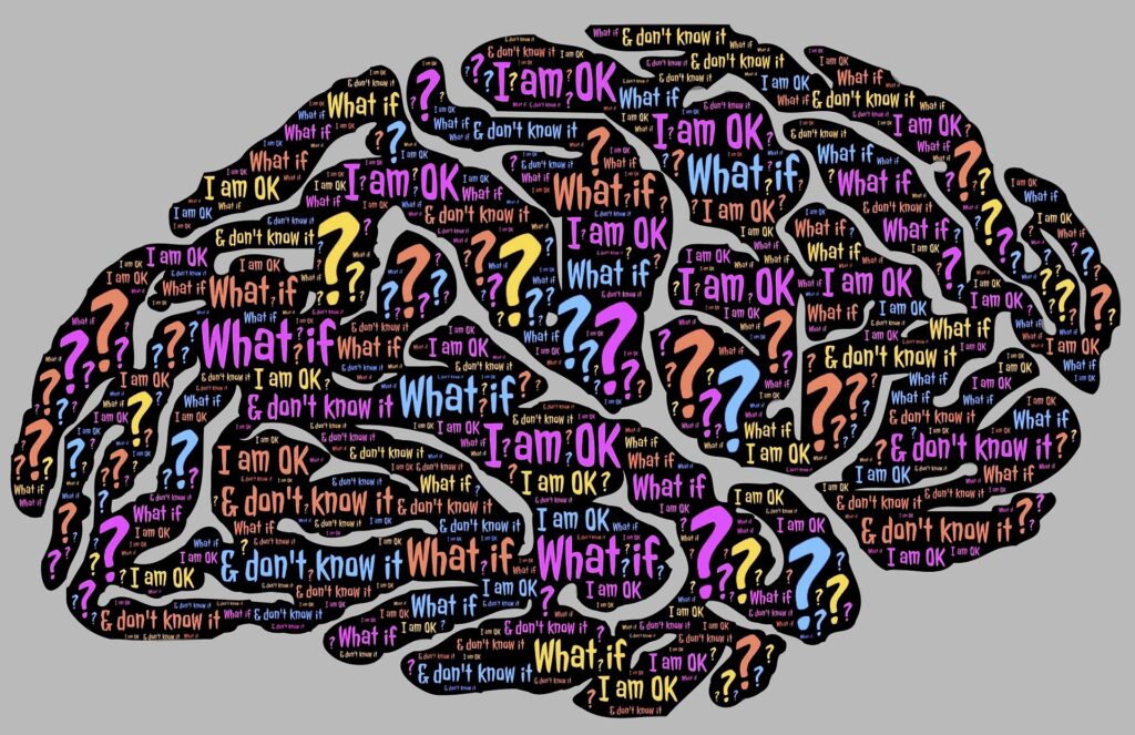 Drawing of a brain made up of multicolor text reading things like "What if" "I am OK" "don't know" and question marks