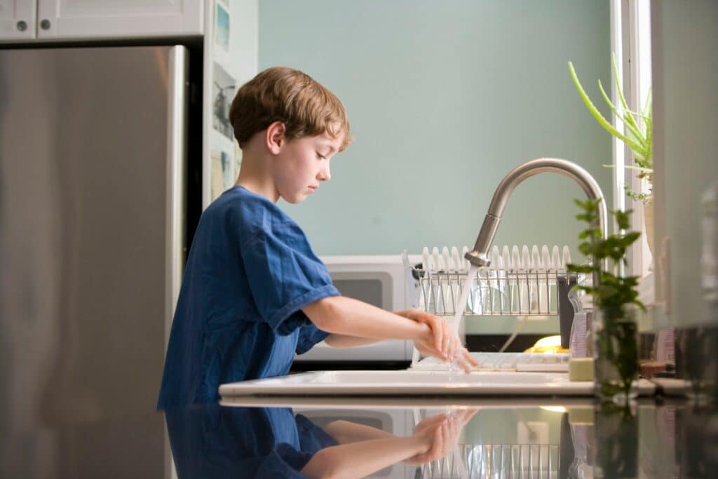 Photo of a young boy in a blue shirt watching his hands in a sink