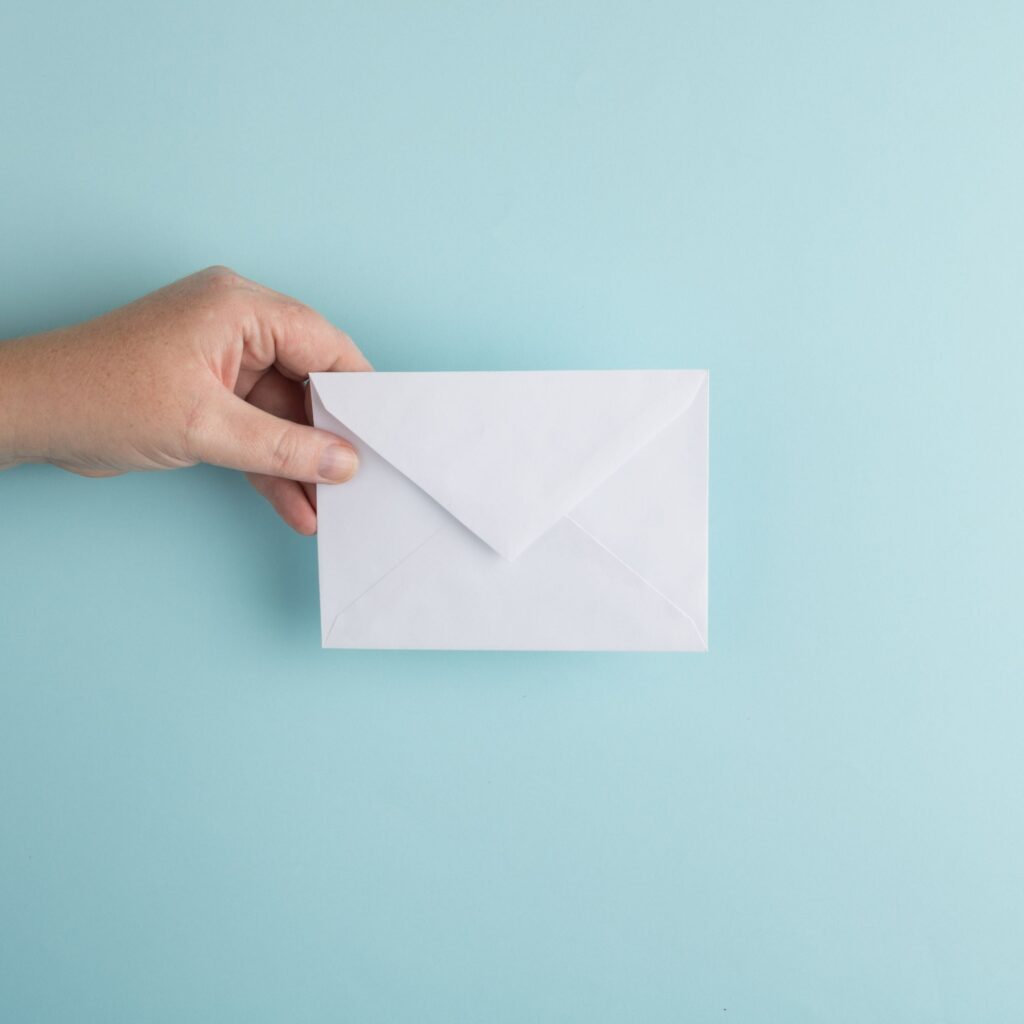 Photo of a hand holding an envelope against a light teal background