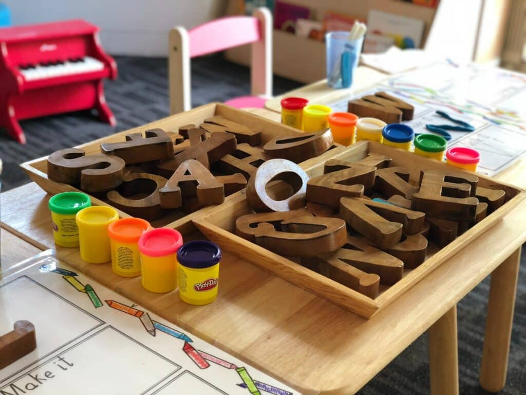 Photo of a desk with jars of different color Play-doh and wooden letter blocks on it. 
