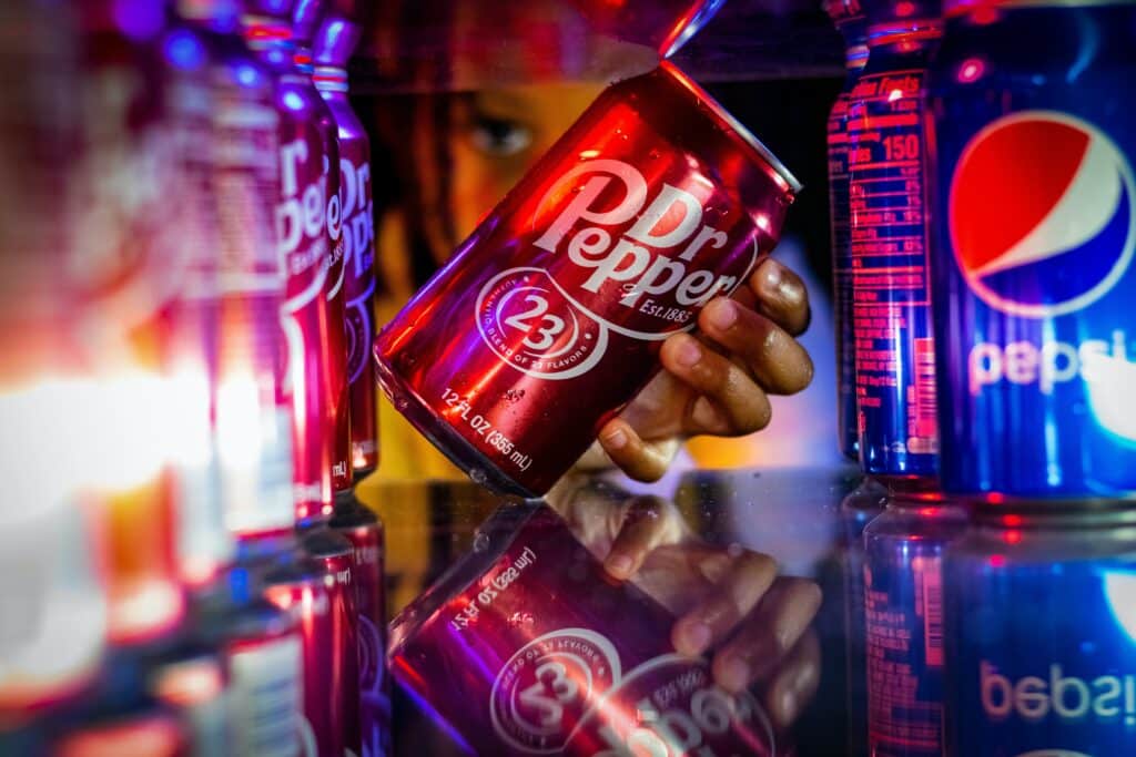 Photo of a person grabbing a can of Dr. Pepper, surrounded by cans of Dr. Pepper and Pepsi