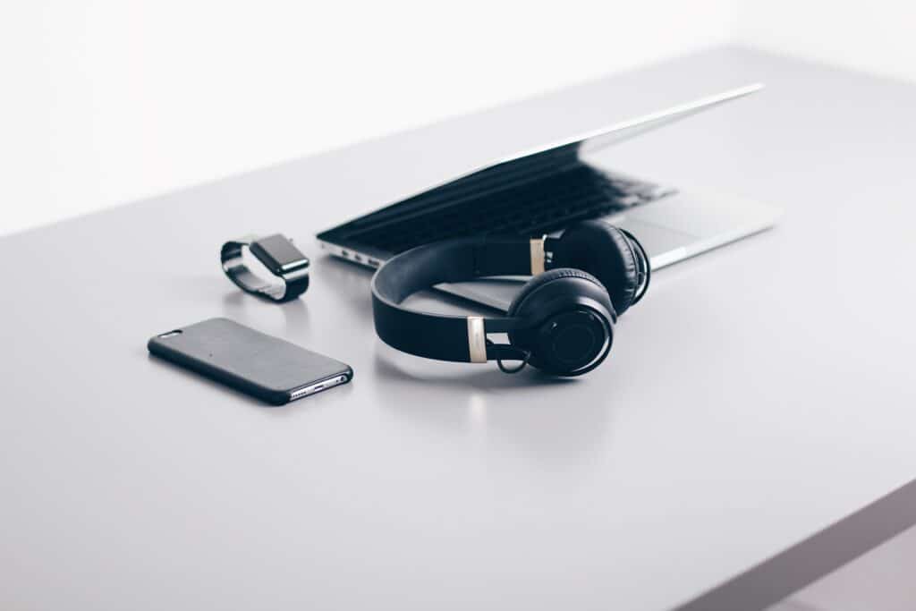 Black headphones, smart phone, watch, and white laptop sitting atop a white table