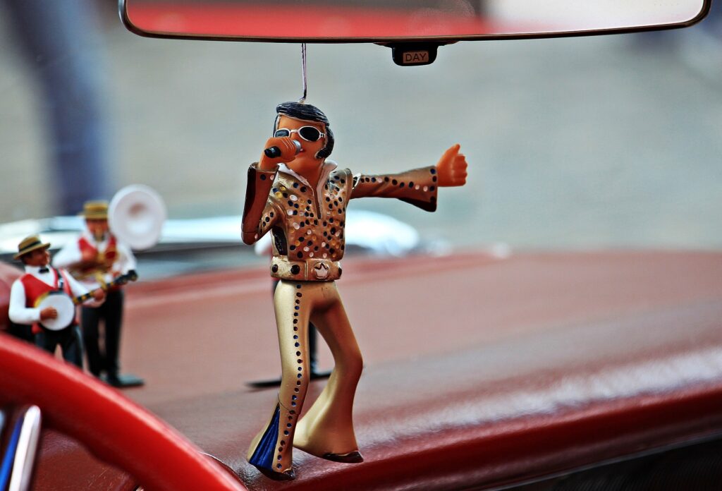 An Elvis Presley ornament hanging from the rear view mirror in a car