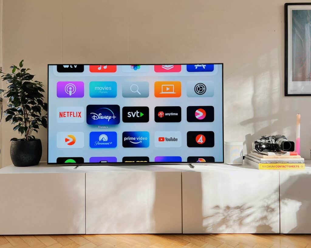 Photo of a large, flat-screen TV displaying numerous streaming apps, atop on a white TV stand. 