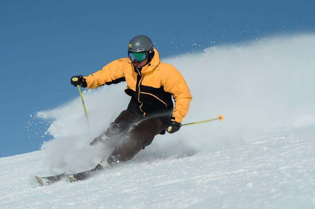 Photo of a man in a yellow and black coat skiing downhill