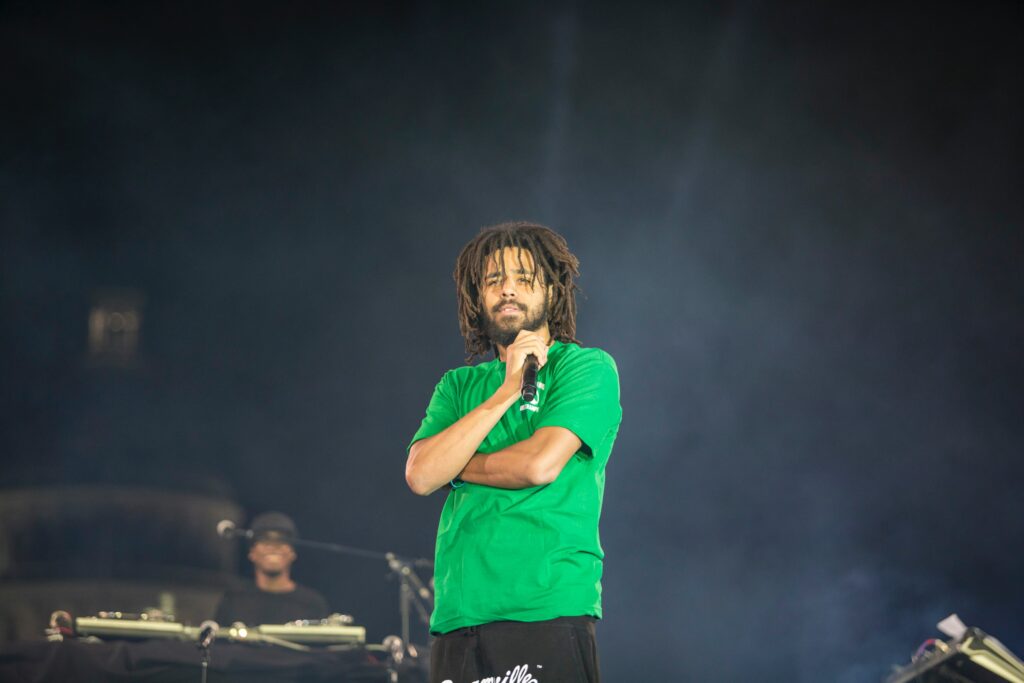 Photo of musician J. Cole in a green t-shirt on stage holding a microphone