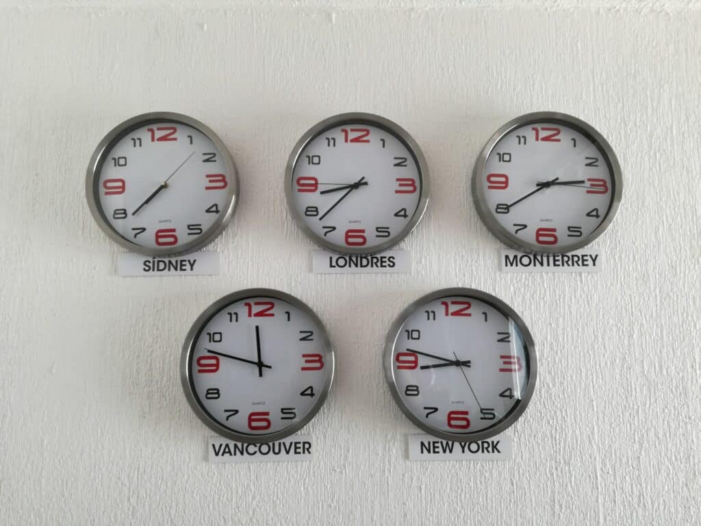 Round analog clocks on a white wall displaying the times of Sidney, Londres, Monterrey, Vancouver, and New York