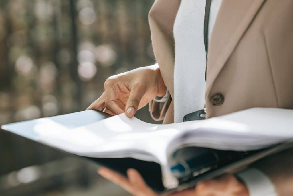 Woman in a white shirt and beige blazer holding open a binder full of papers