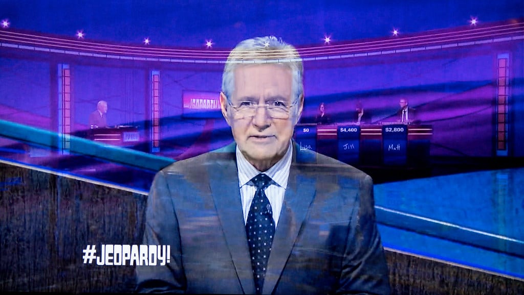 Photo of Alex Trebek overlayed with another image of him hosting Jeopardy! in the background.