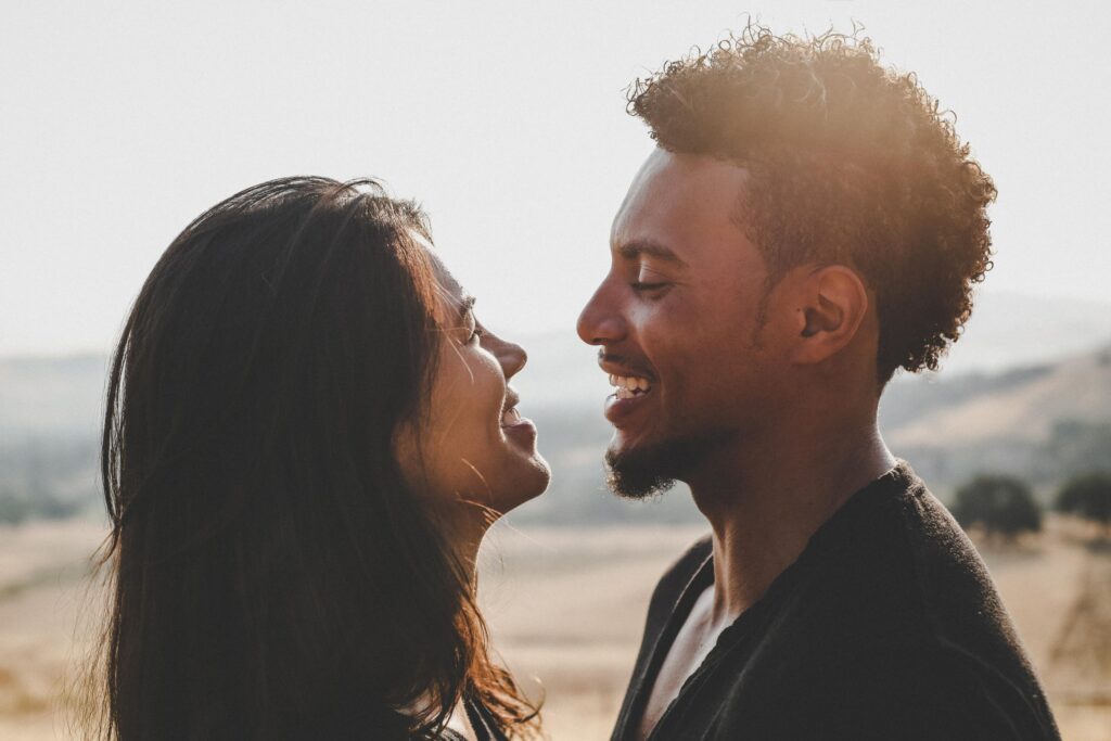 Photo of a couple smiling at each other with mountains in the background.