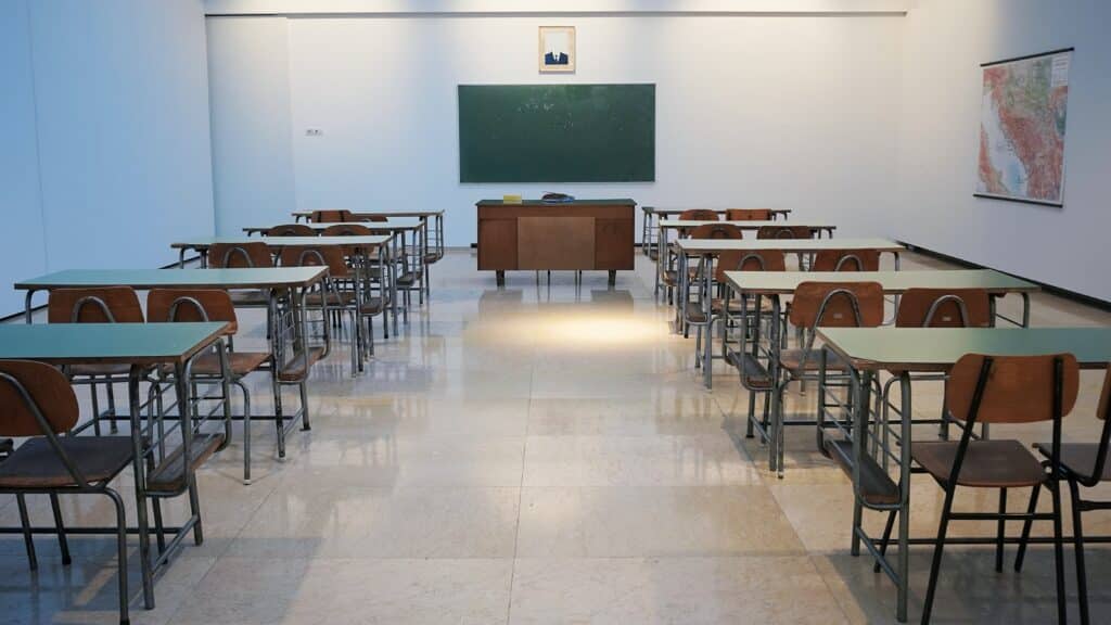 Photo of an empty classroom with desks, a large blackboard in the background, and a map on the wall.