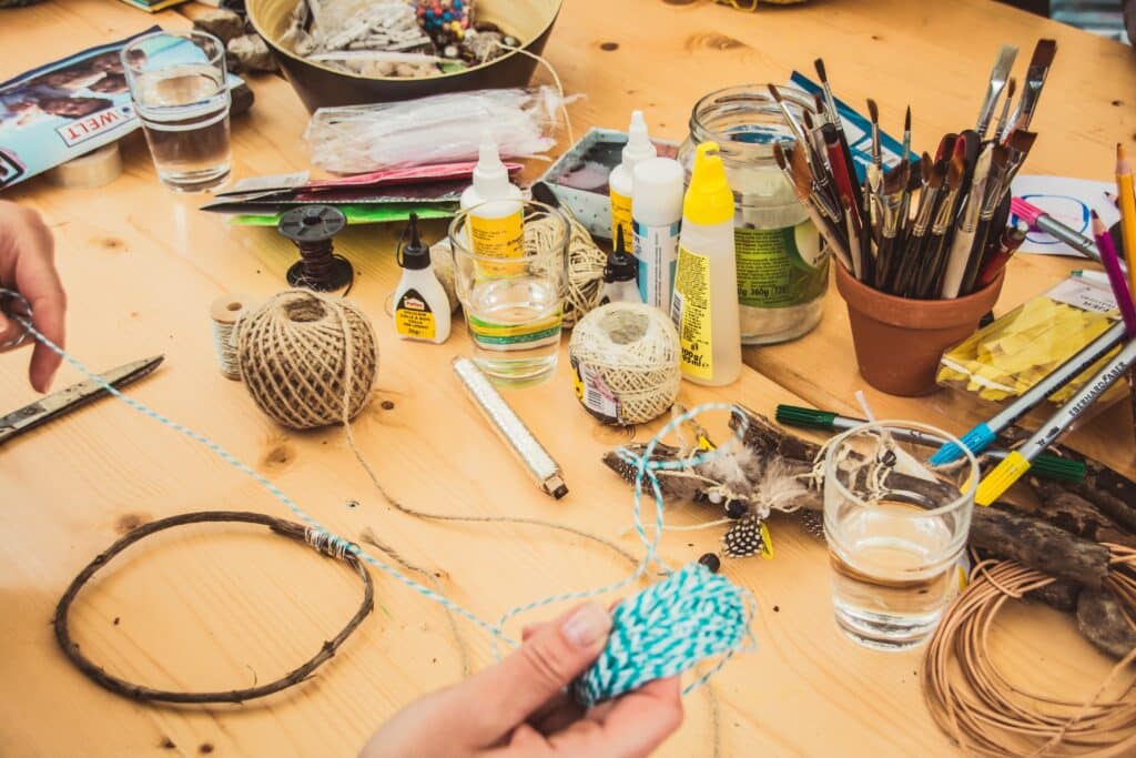 Photo of various crafts and craft materials on a wooden table with a person's hands holding yarn