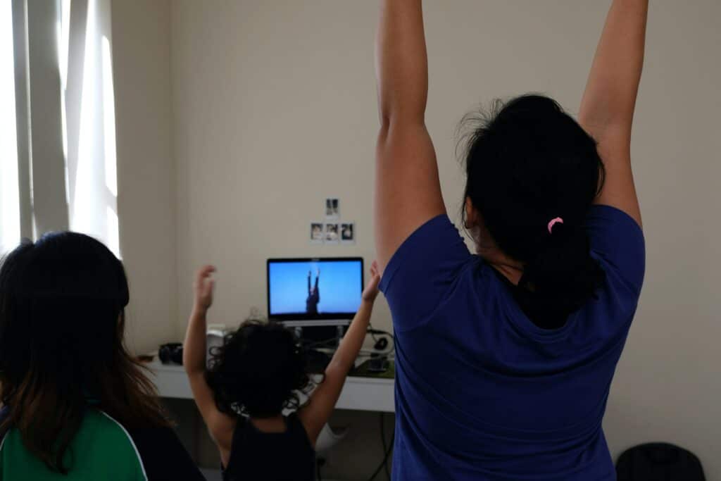 Photo of a family celebrating or exercising, arms in the air, while watching a woman on TV do the same. 