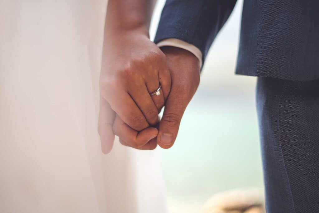 Close up photo of a bride and groom's hands held together, showing the bride's wedding ring.