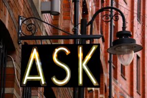 Photo of an illuminated sign on a street lamp that reads "ASK"