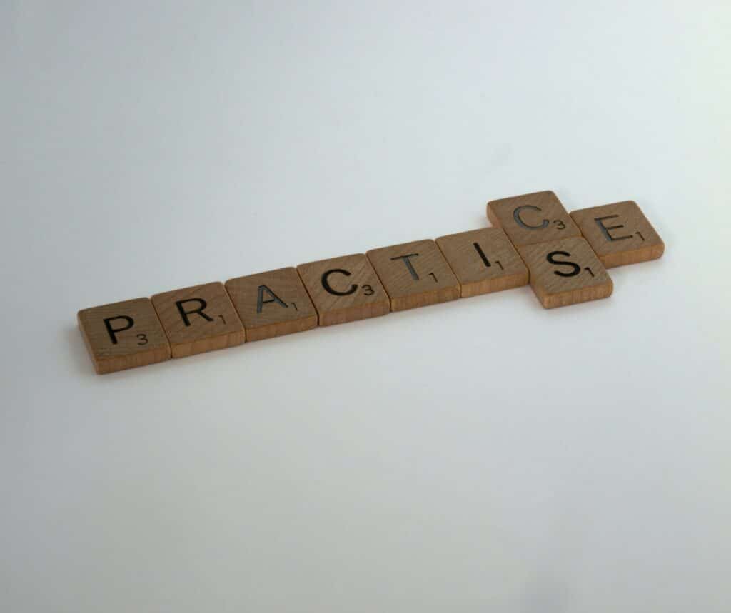 Wooden Scrabble blocks spelling out two different spellings of Practic(s)e.