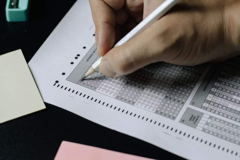Photo of a person's hand using a white pencil to fill out a Scantron-style exam answer selection sheet.