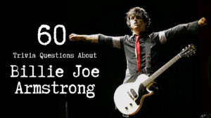 Photo of Green Day frontman Billie Joe Armstrong on stage, his arms spread apart. He's wearing a black button-down shirt with a red tie and has a white guitar on his shoulder, against a black background. White text next to him reads "60 Trivia Questions About Billie Joe Armstrong."