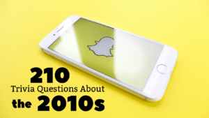 Photo of a white iPhone displaying the Snapchat loading screen, with the app's ghost logo, against a yellow background. Text under it in black reads "210 Trivia Questions About the 2010s."