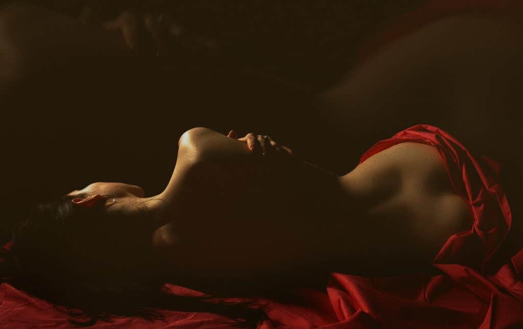 Photo of the back of a woman draped in red silk sheets, lying down.