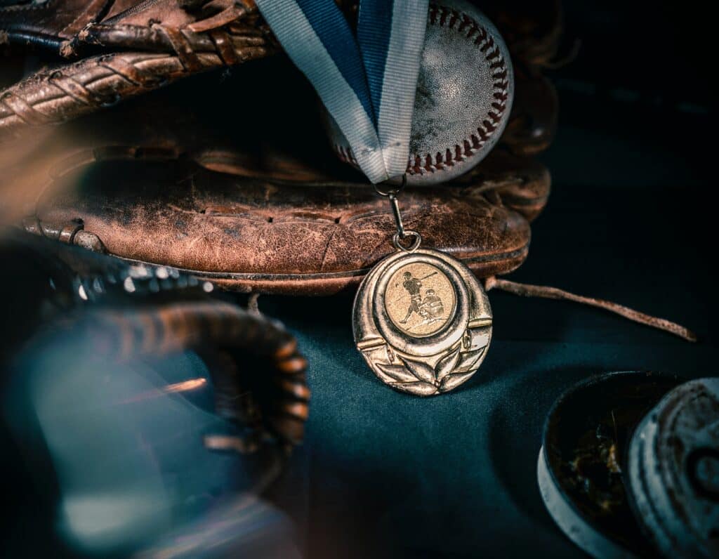 Close up photo of a baseball gold medal against a baseball in a baseball mitt.