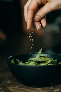 A hand salting peas in a black bowl