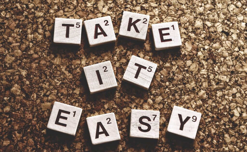 Scrabble tiles spelling out "TAKE IT EASY" against a corkboard texture background.