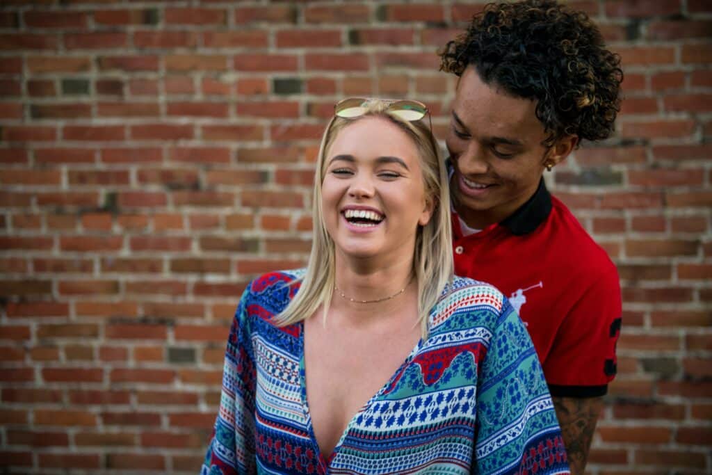 Photo of a couple laughing in front of a brick wall.