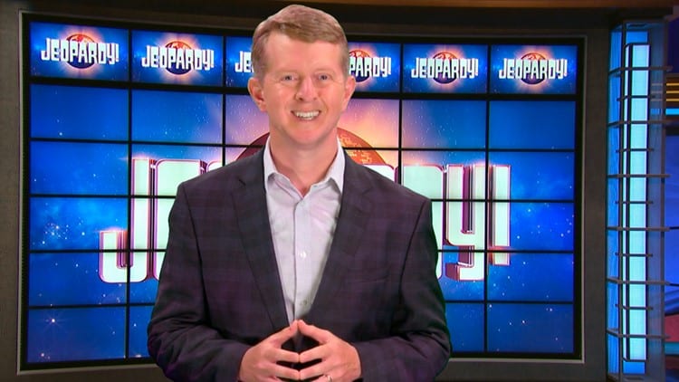Photo of Ken Jennings standing in front of the Jeopardy! board. 