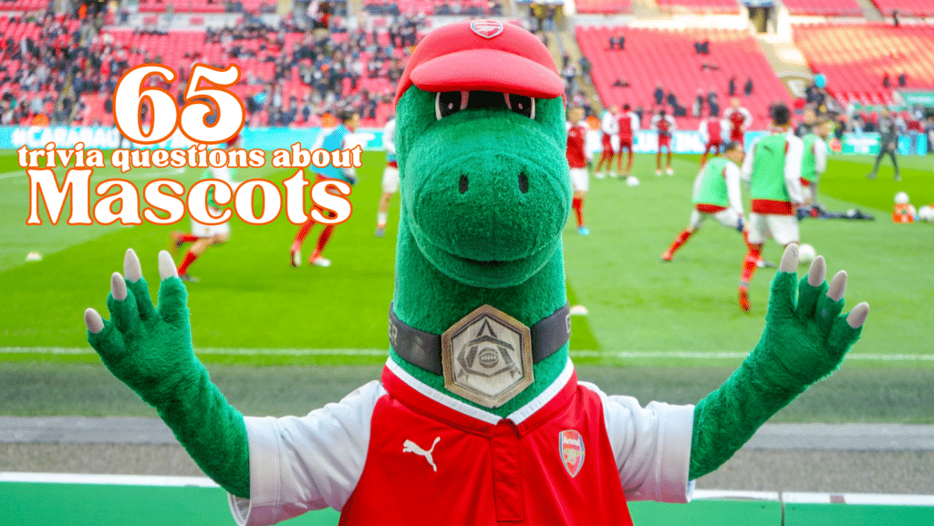 Photo of a green dragon mascot in a red cap and jersey in front of a game on a soccer field.