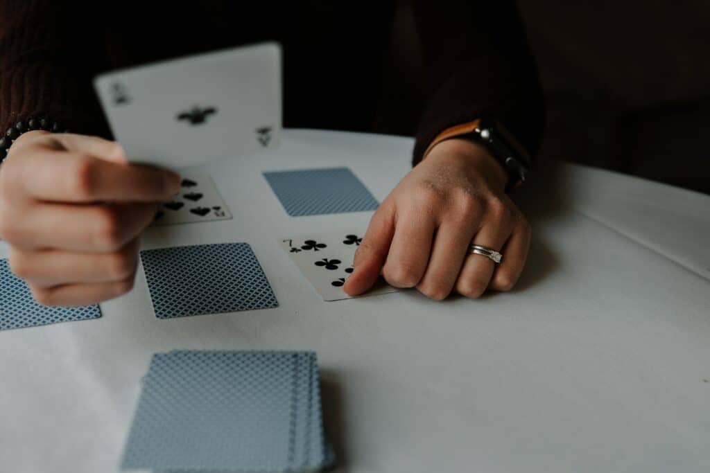Photo of a person's hands playing a game of solitaire on a white table. 