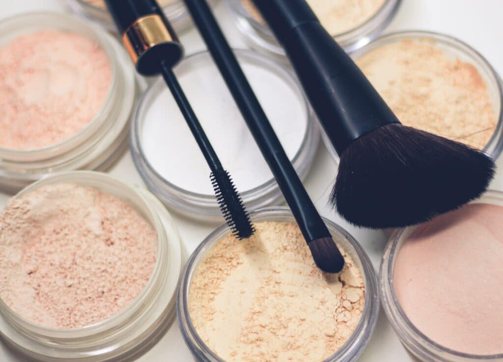 Photo of various powders and face makeup with three black makeup brushes atop them.