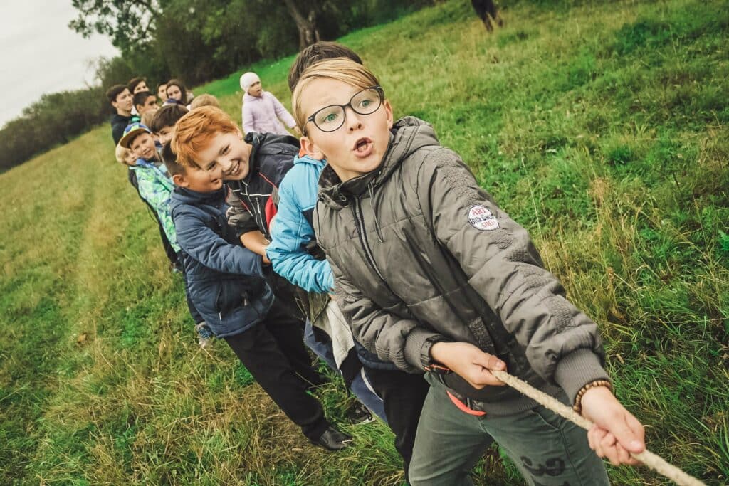Photo of a group of kids playing tug of war in a large, grassy field. 
