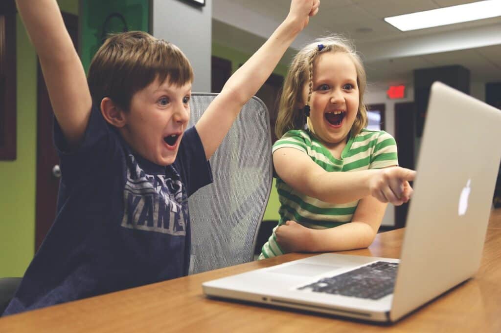 Photo of two kids, a boy and a girl, cheering and pointing at an Apple laptop.