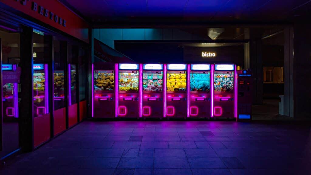 Photo of a row of neon-lit vending and claw machines in a dark room.