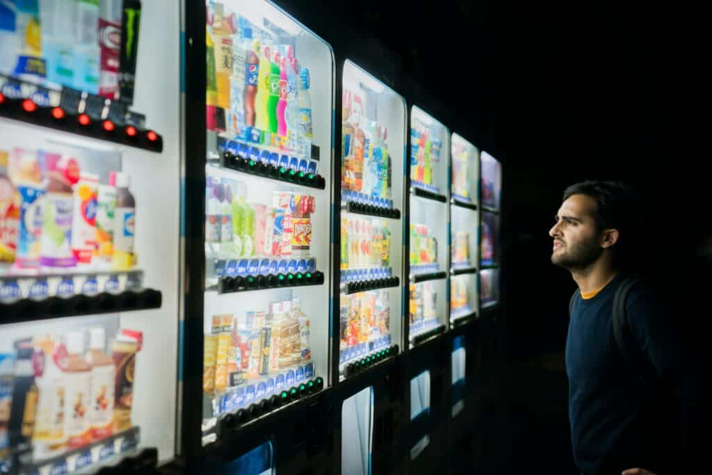 Photo of a man in a black shirt staring at many options in brightly-lit vending machines.